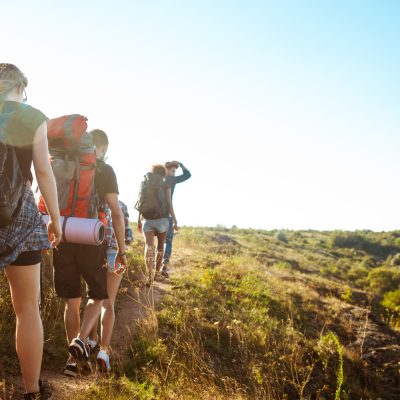 Young beautiful friends travelers with backpacks walking in canyon. Copy space.